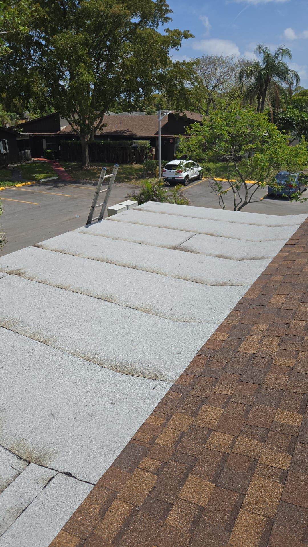 View from a roof showing white concrete blocks, a ladder, and cars parked in a lot behind the building.