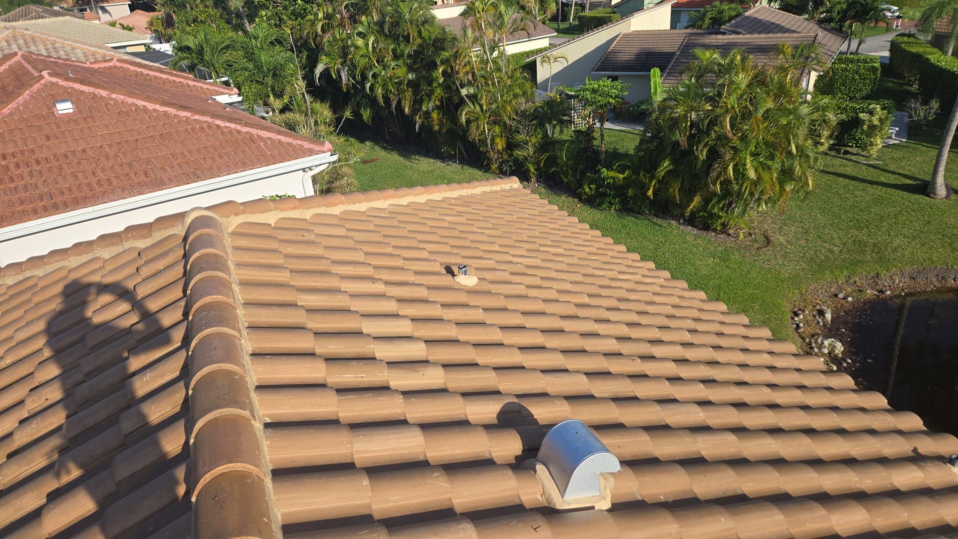 A view of a brown tile roof with a shadow of a person taking a photo.