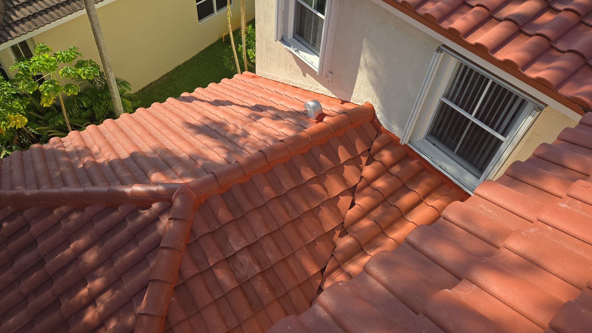 Overhead view of a red tile roof on a light-colored house with two windows. Sunny outdoor setting.