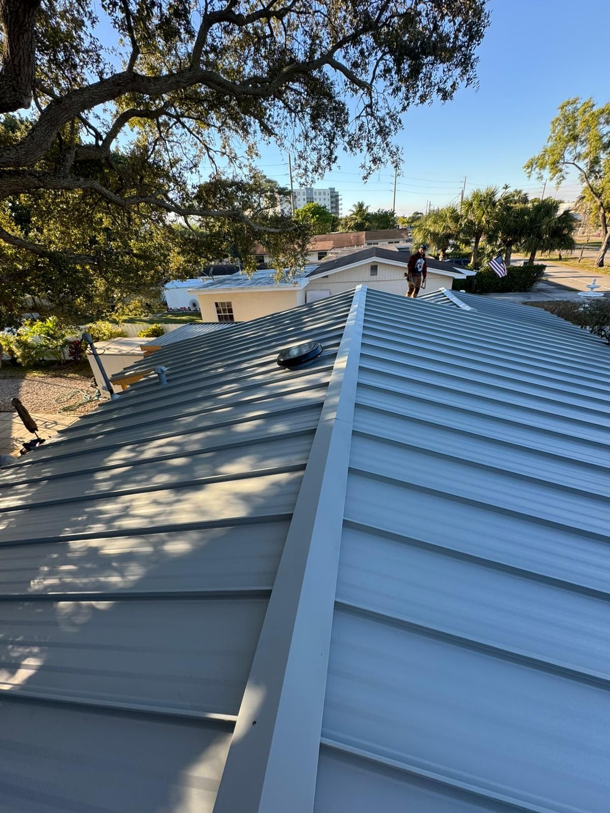 A metal roof with light gray panels, a white trim, and workers in the background. 