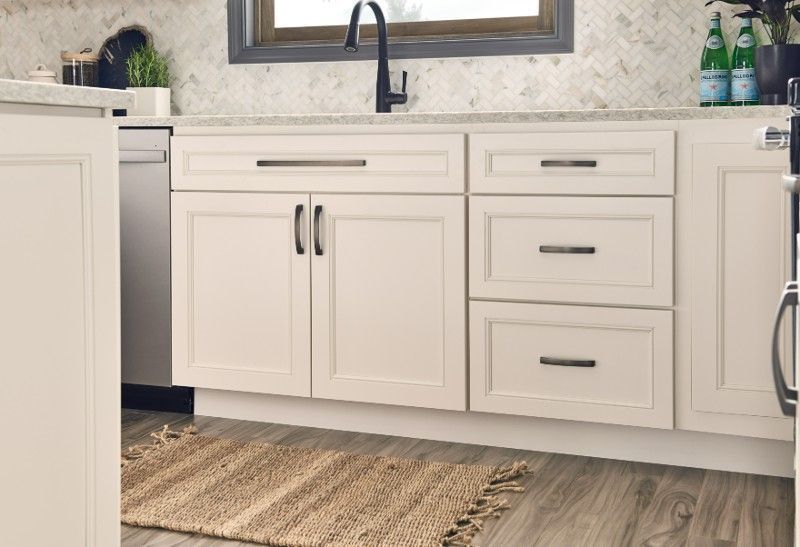 A kitchen with white cabinets , drawers , a sink and a rug.