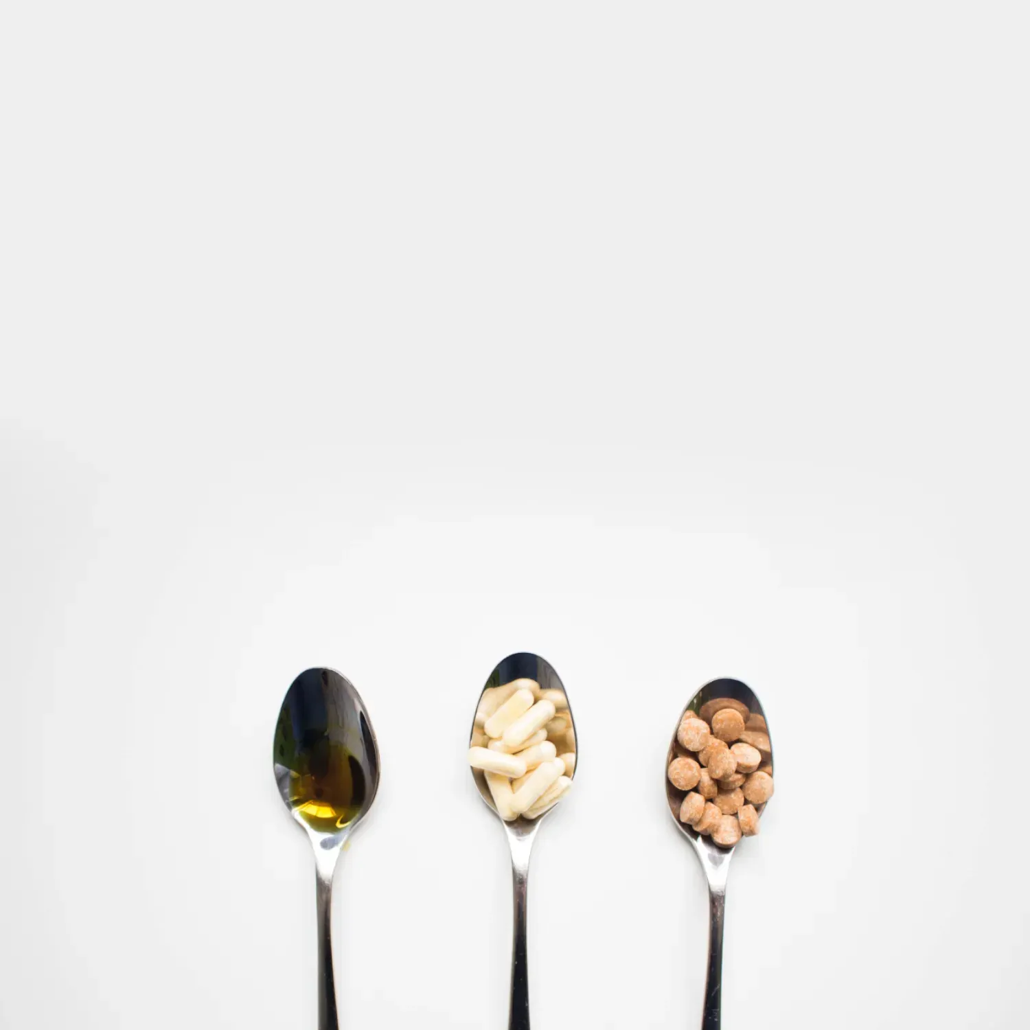 three spoons carrying oil, capsules and nuts