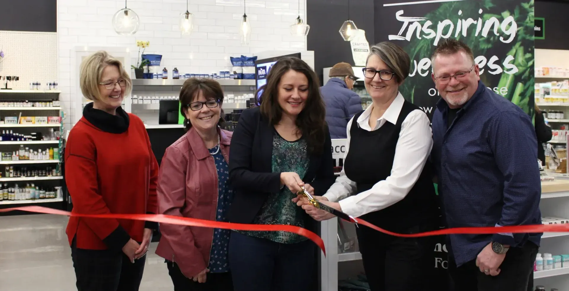 A group of people cutting a line of red tape for a Grand Opening