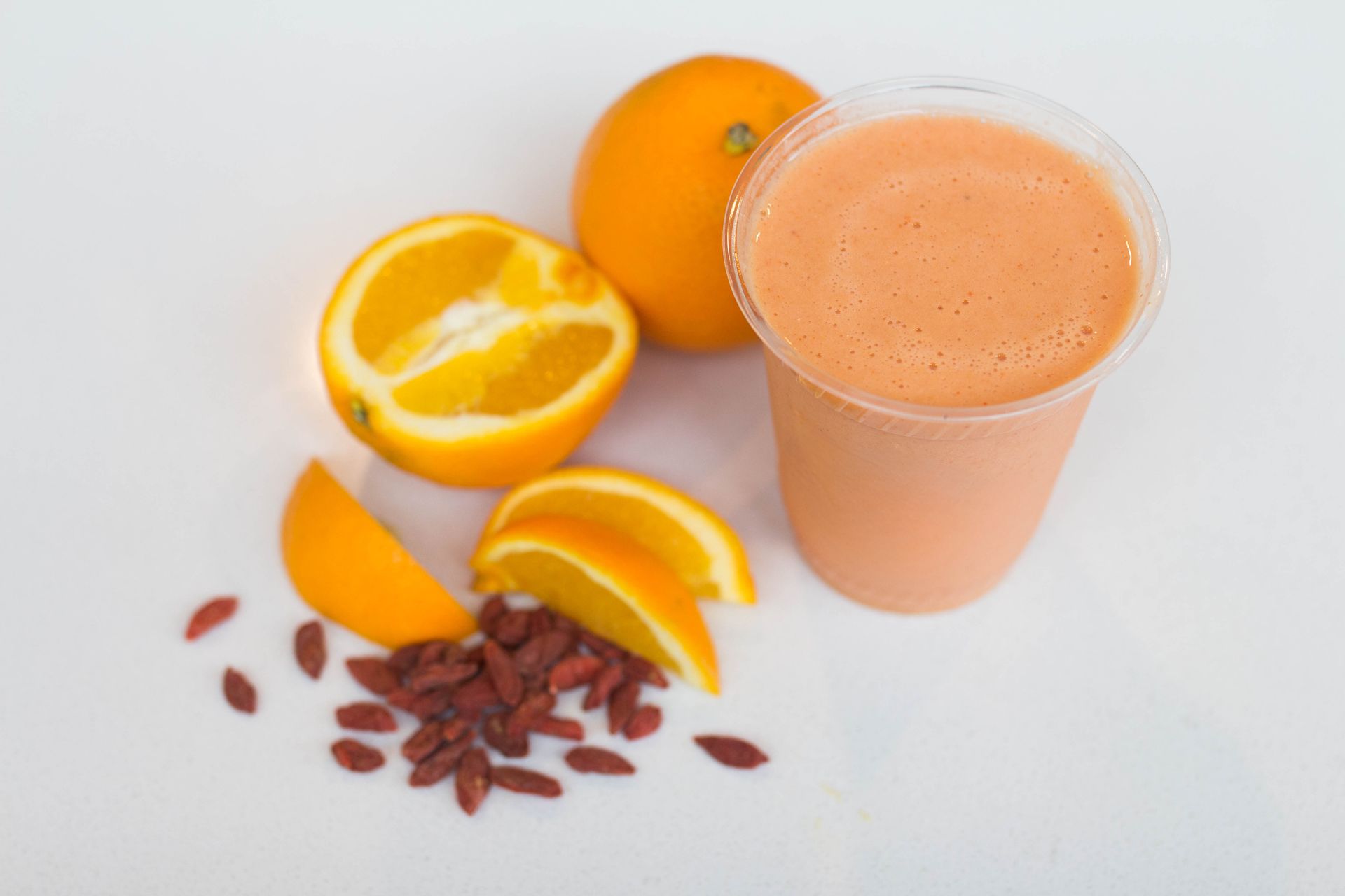 orange smoothie in a cup with a sliced orange and goji berries next to it