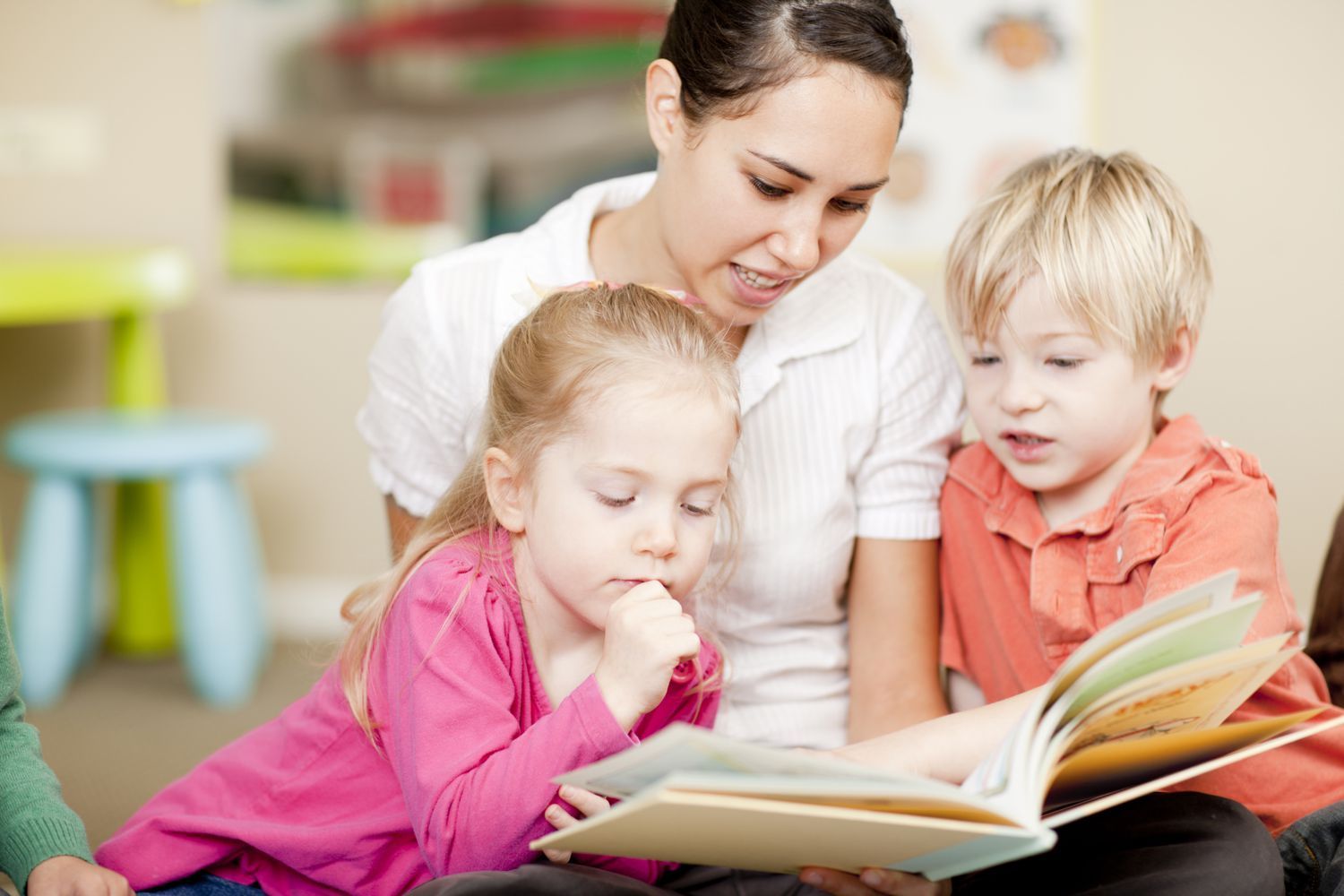 two children reading a book with an adult