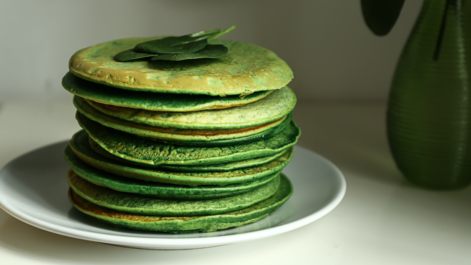 stack of green spinach pancakes on a white plate