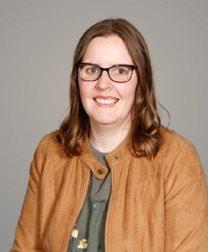 A woman wearing glasses and a scarf is smiling for the camera.