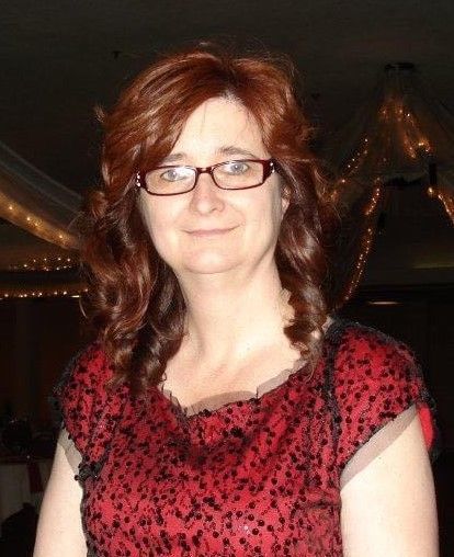 A woman wearing glasses and a red shirt is smiling for the camera.