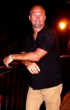 A man in a black shirt is standing in the dark with his arms crossed.