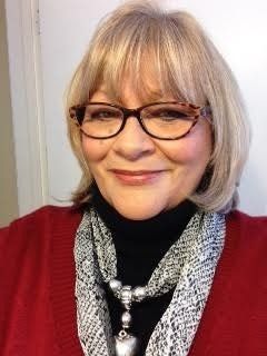 A woman wearing glasses and a scarf is smiling for the camera.