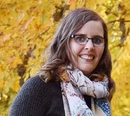 A woman wearing glasses and a scarf is smiling for the camera.