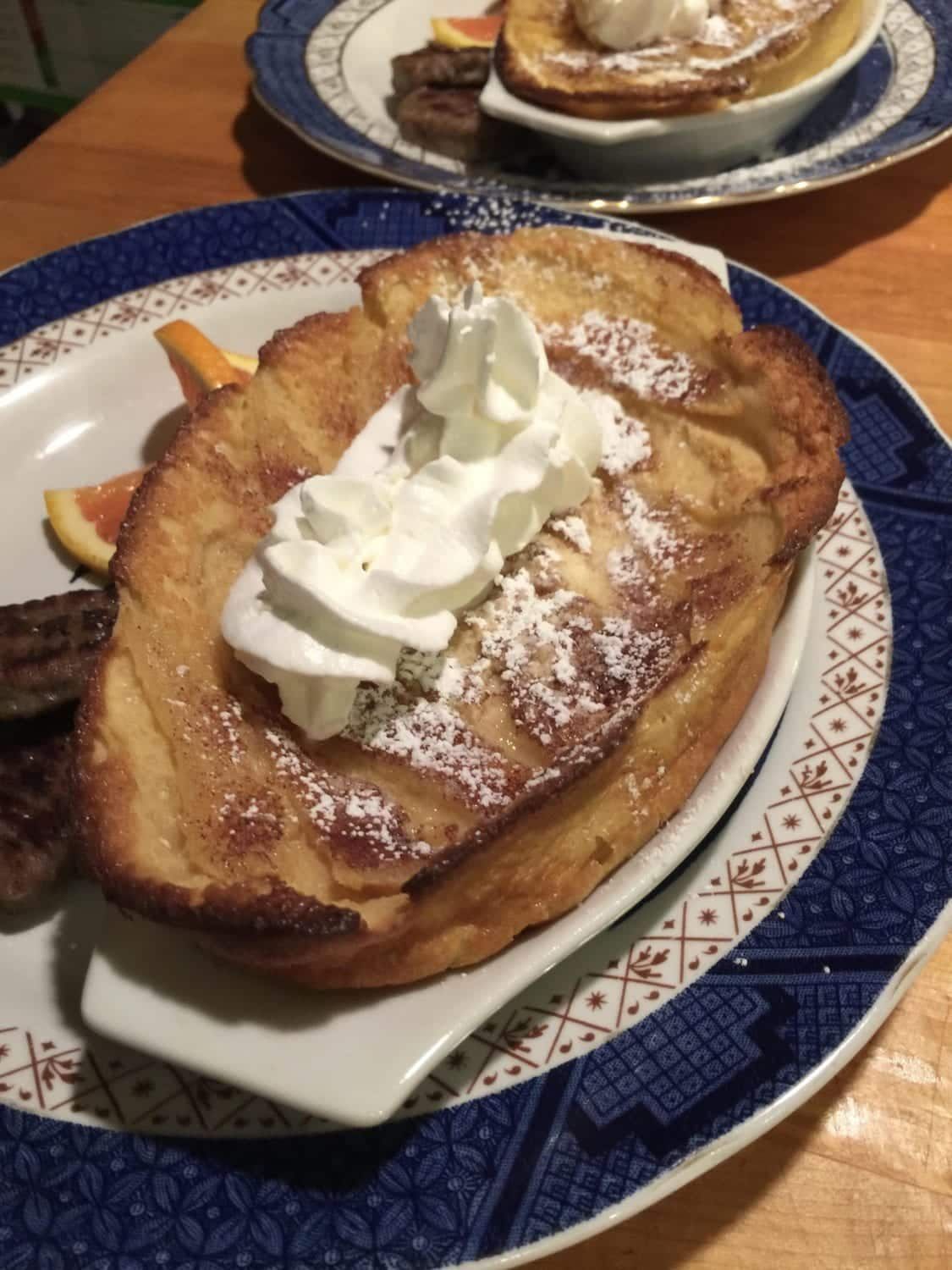 French toast with whipped cream and powdered sugar on a blue plate