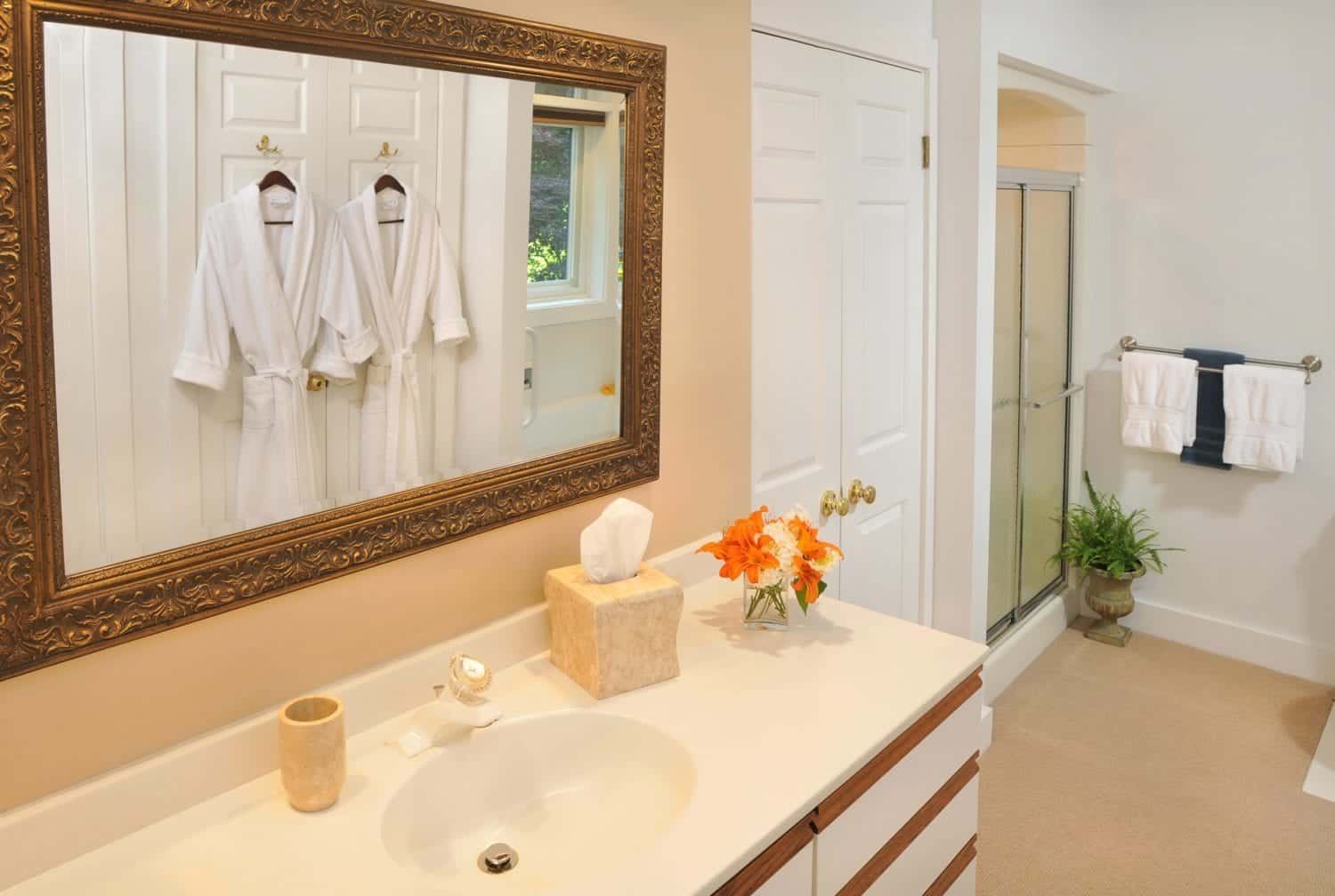 A bathroom with a sink , mirror and robes hanging on the wall