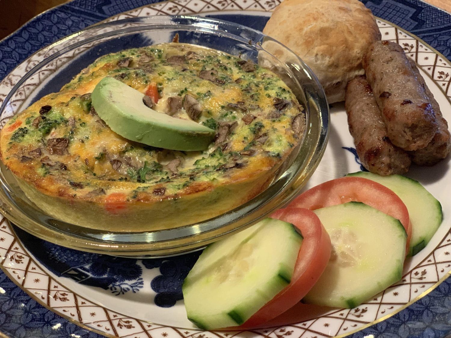 A plate of food with a quiche tomatoes cucumbers and sausages