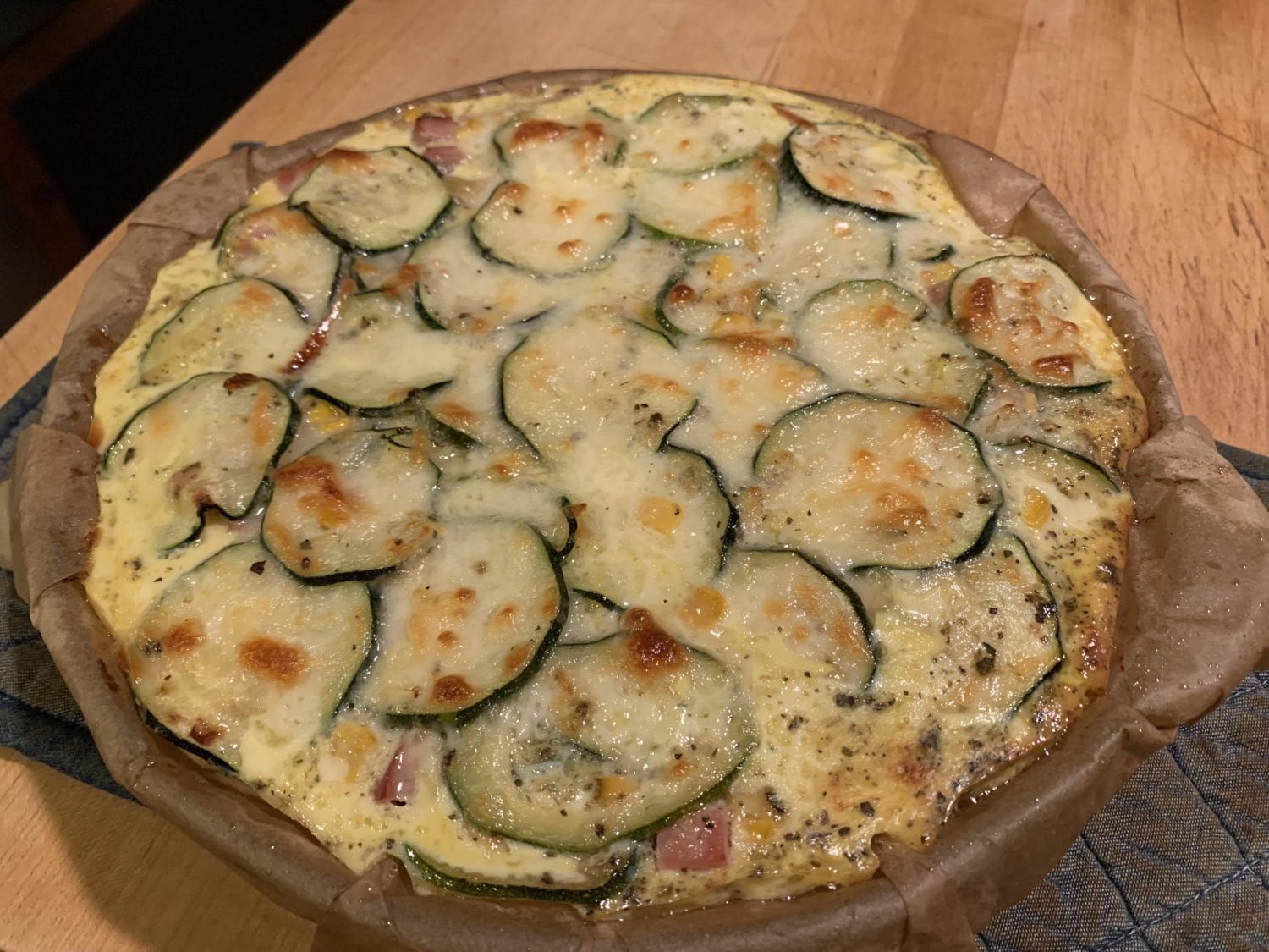 A pizza with zucchini and cheese on a wooden table.