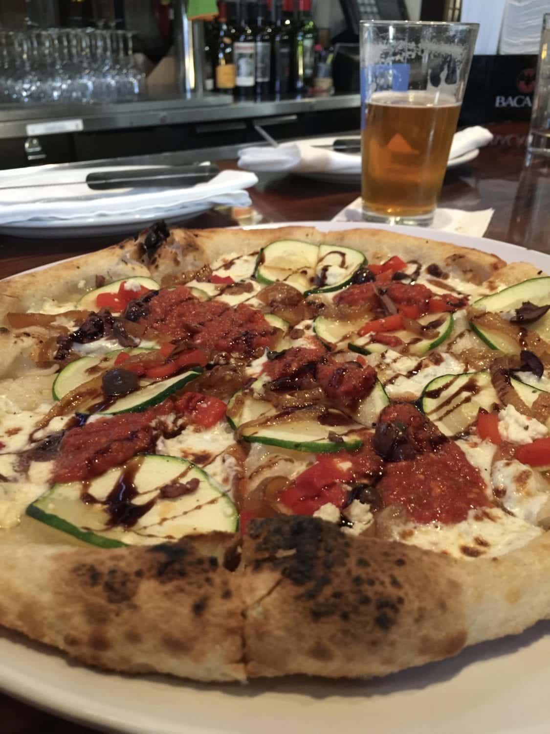 A pizza on a plate with a glass of beer in the background