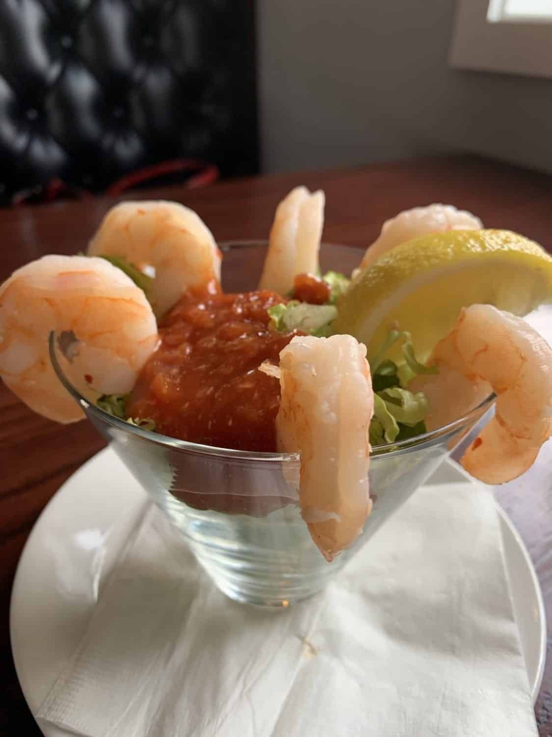 A shrimp cocktail in a martini glass on a napkin on a table.