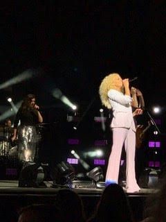 A woman in a white suit is singing into a microphone on a stage.