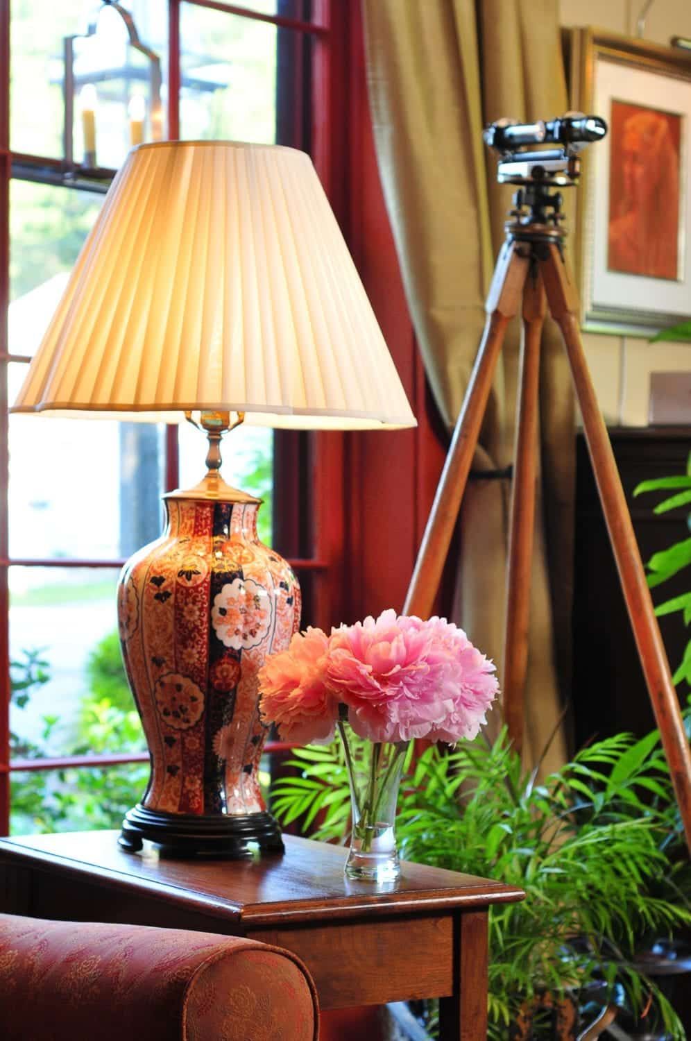 A lamp sits on a table next to a vase of pink flowers