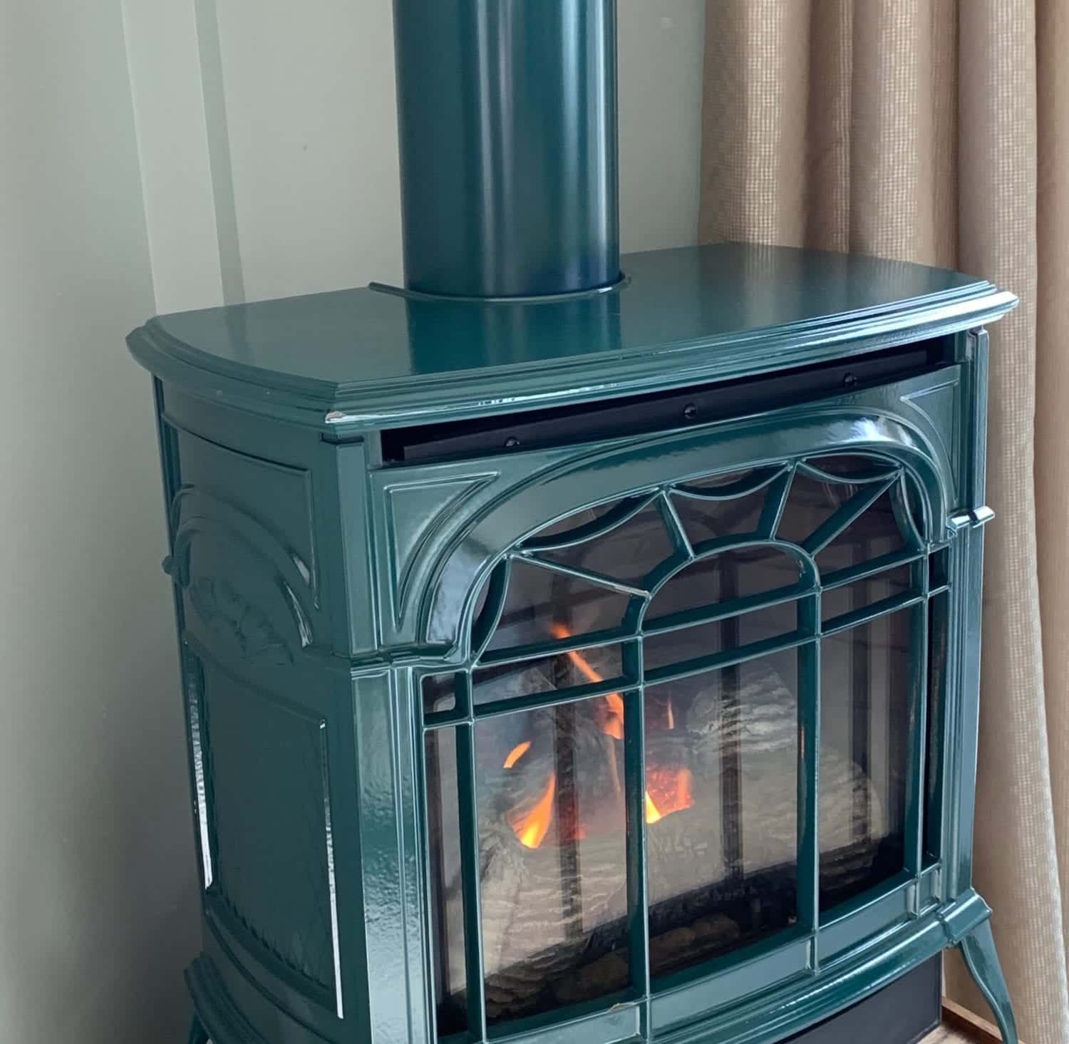 A green wood stove is sitting in a room next to a window.