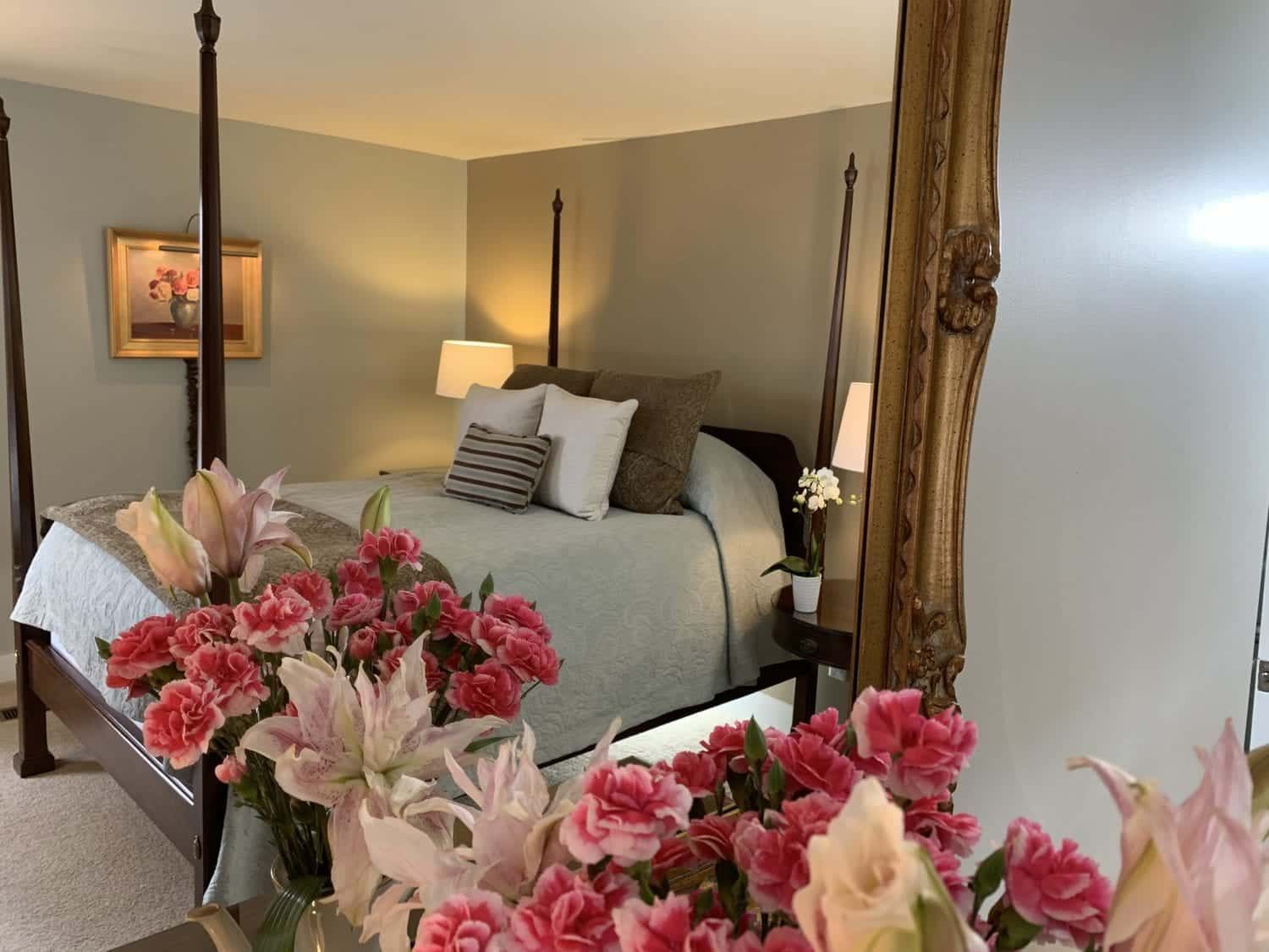 A bedroom with a four poster bed and flowers in front of a mirror.