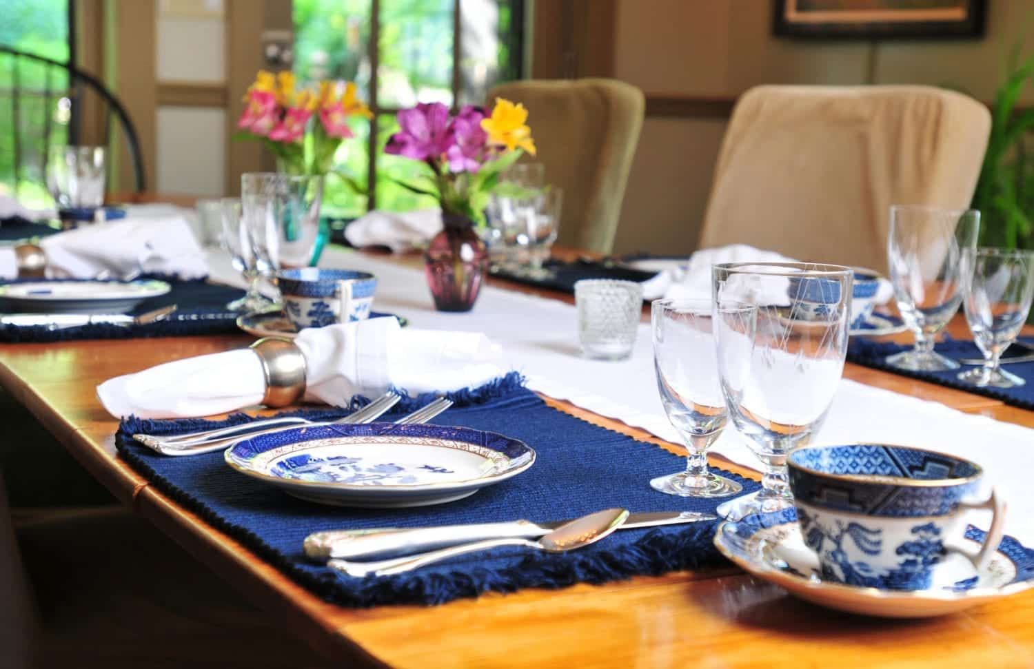 A table set for a meal with plates , cups , glasses and flowers on it.