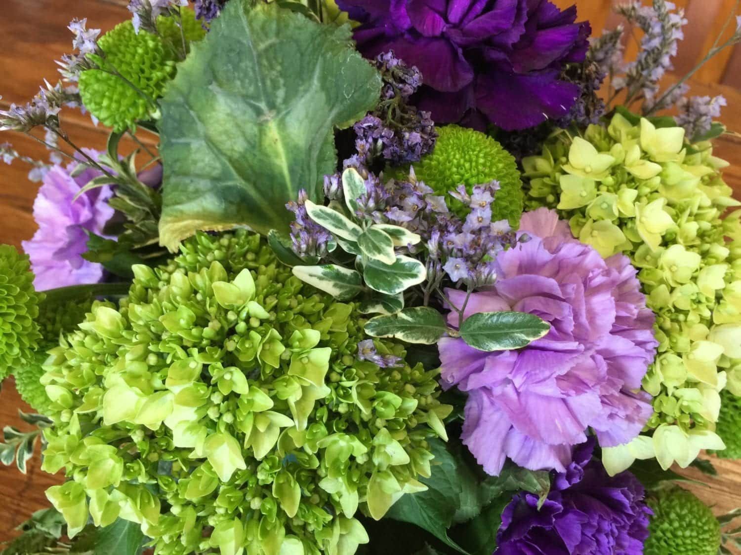 A close up of a bouquet of purple and green flowers on a wooden table.