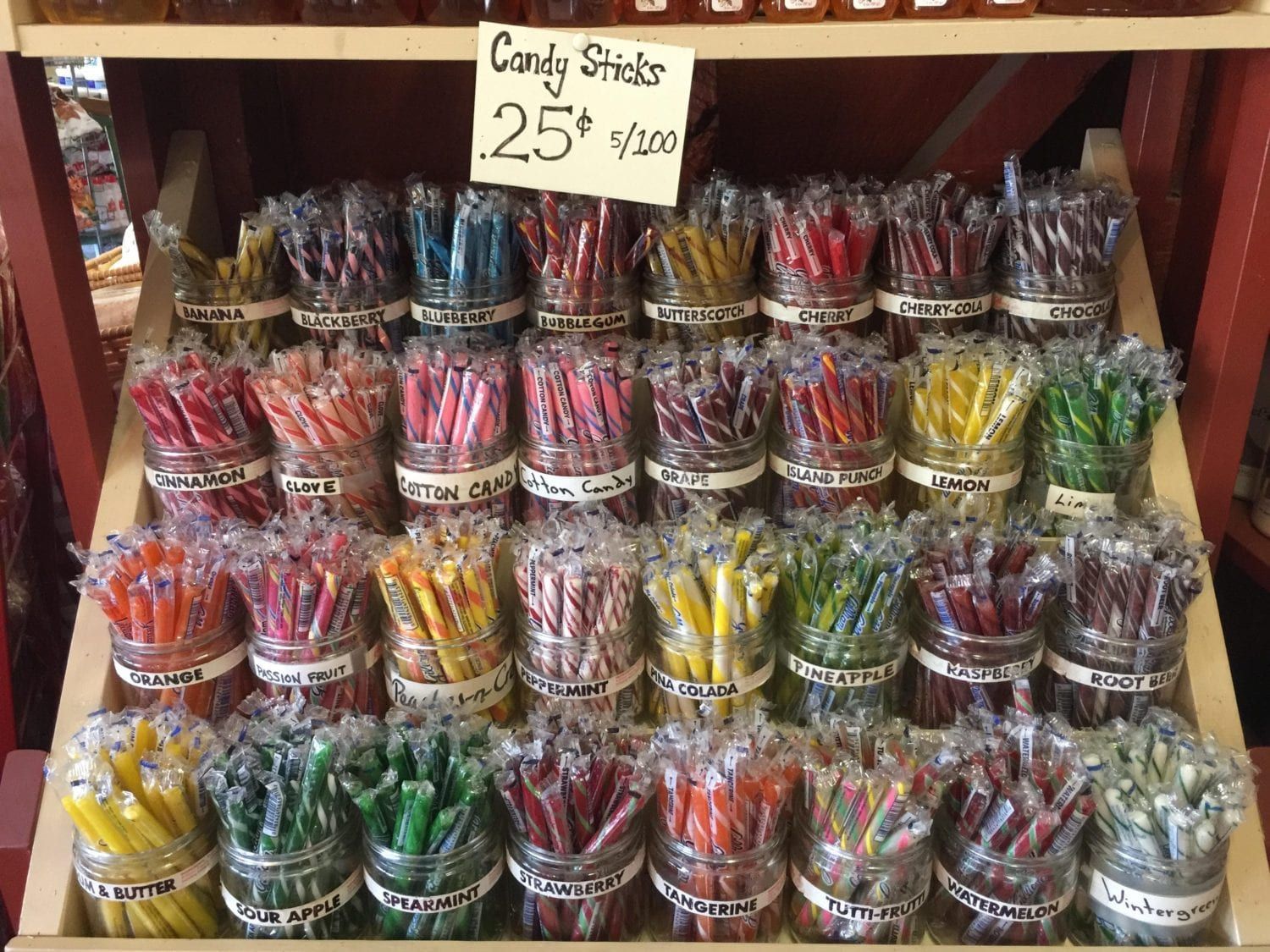 A display of candy sticks in jars on a shelf.
