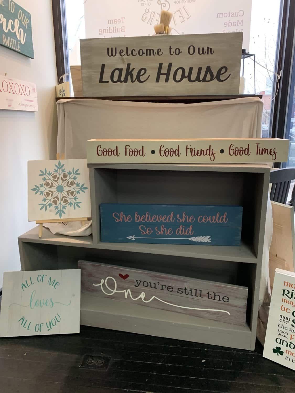 A shelf filled with wooden signs and a sign that says welcome to our lake house.