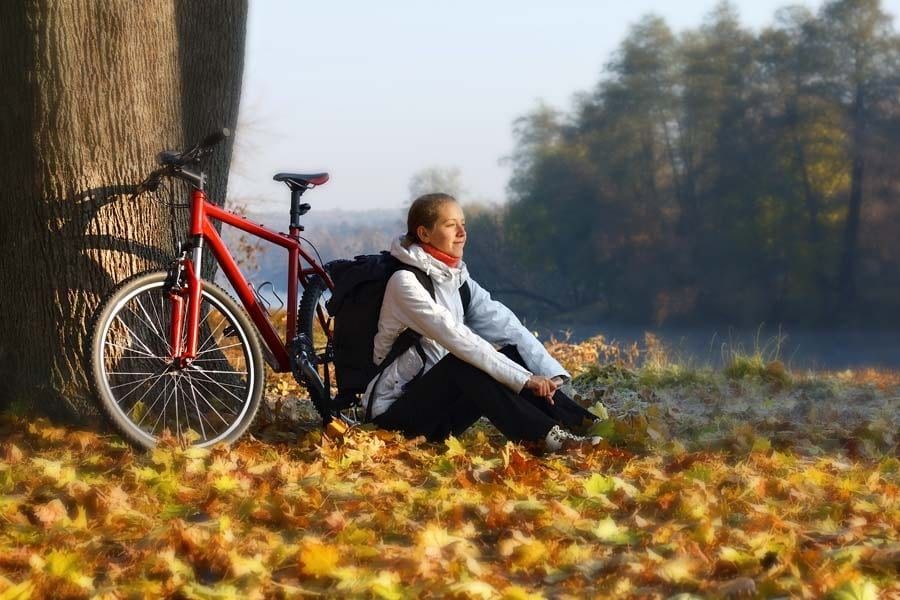 A woman is sitting next to a bicycle leaning against a tree.