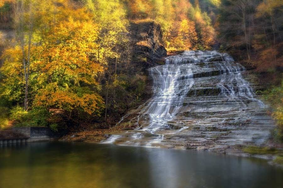 A waterfall is surrounded by trees and a lake in the middle of a forest.
