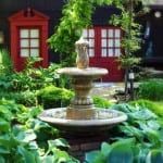 A fountain in a garden in front of a red phone booth.