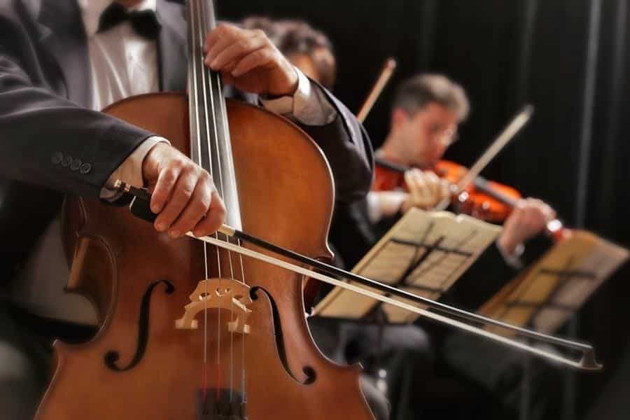 A man in a suit is playing a cello in an orchestra.