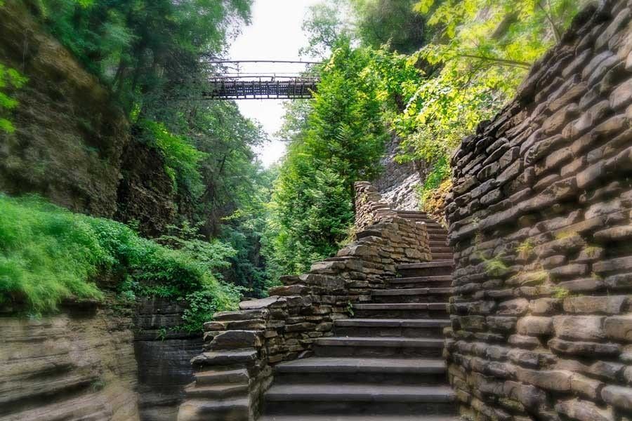 A stone wall with stairs leading up to a bridge in the background.