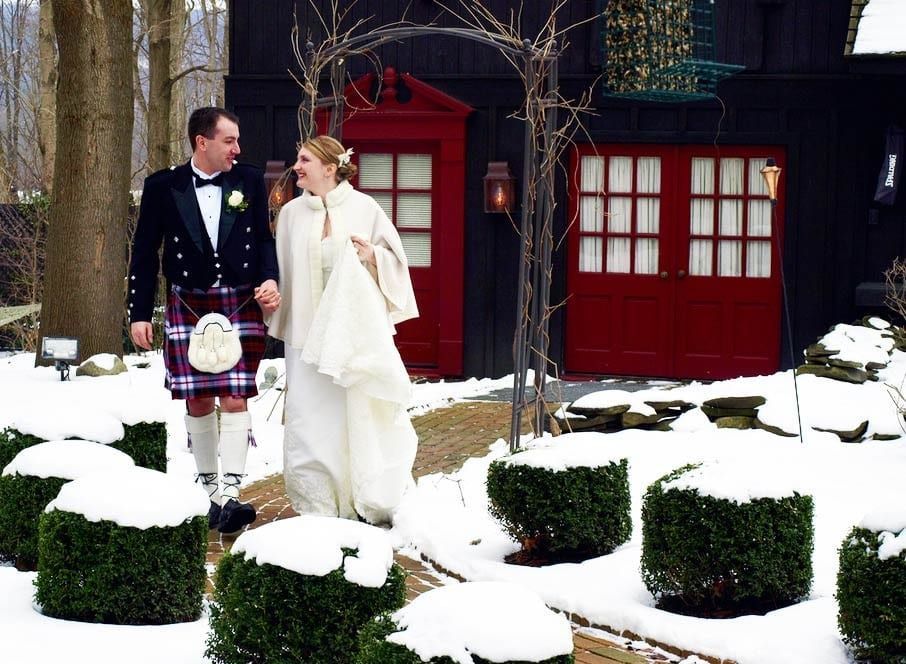 A bride and groom are walking in the snow in front of a red garage door