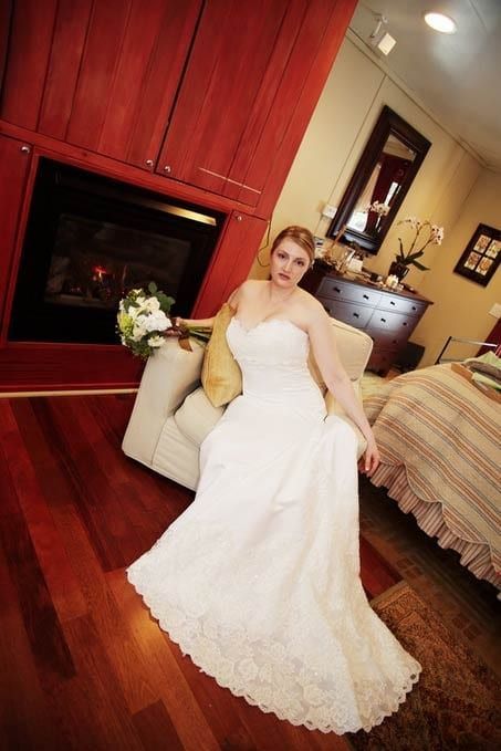 A woman in a wedding dress is sitting in a chair in front of a fireplace.