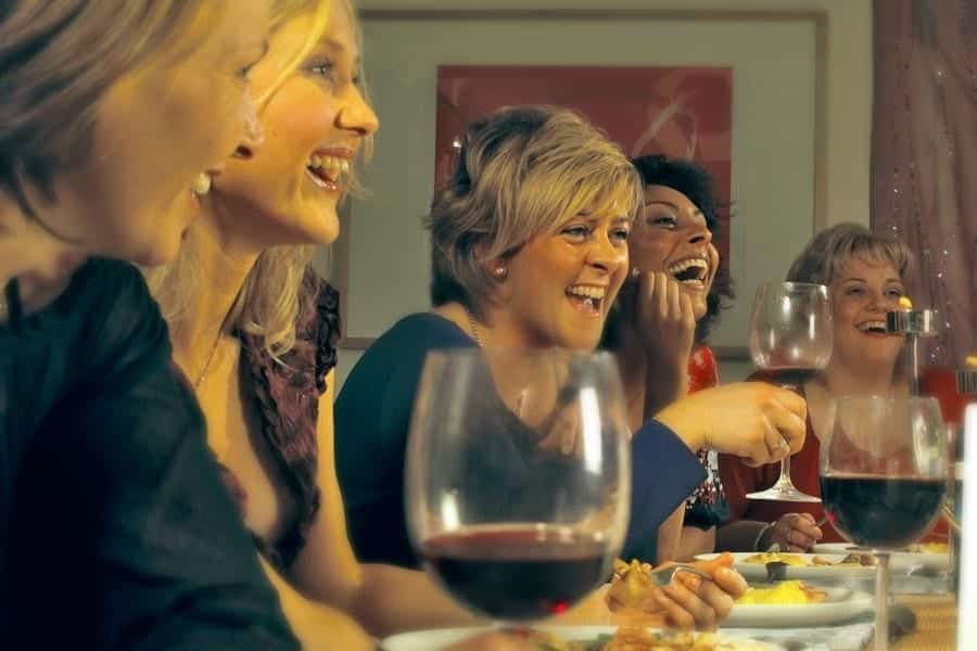 A group of women are sitting at a table drinking wine and laughing.