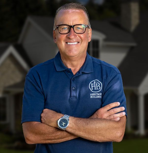 Man in blue polo shirt with crossed arms, smiling; building backdrop.