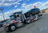 American flag-themed tow truck towing a white box truck on a city street.