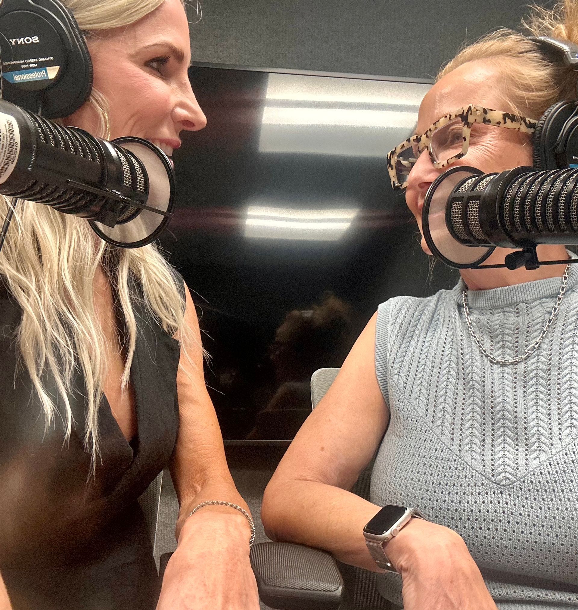 Two women in a podcast studio talking into microphones and smiling across a table.