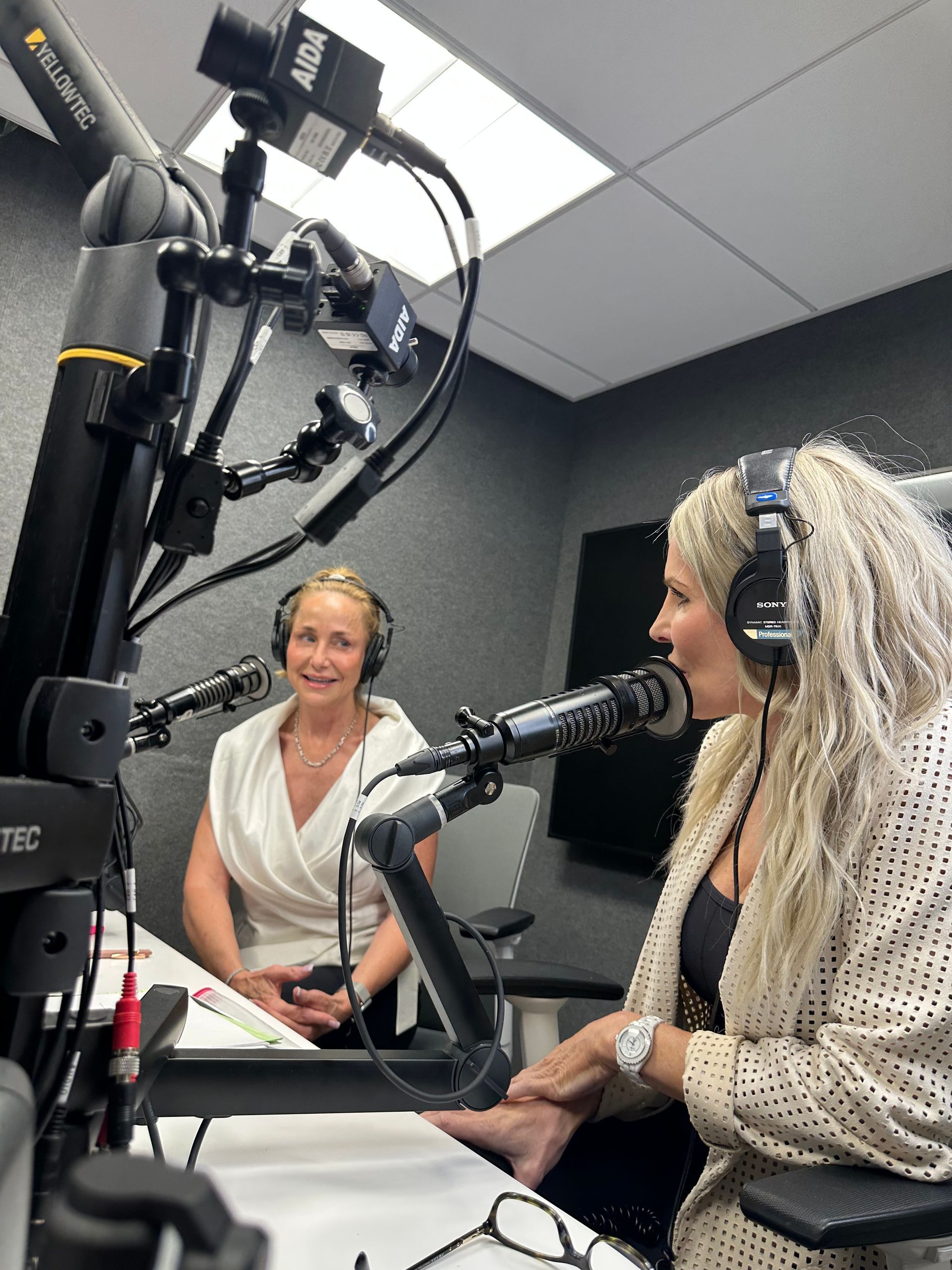 Two women podcasting in a studio, speaking into microphones while wearing headphones.