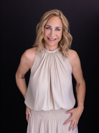 Smiling woman in a beige halter top and skirt, standing against a dark background