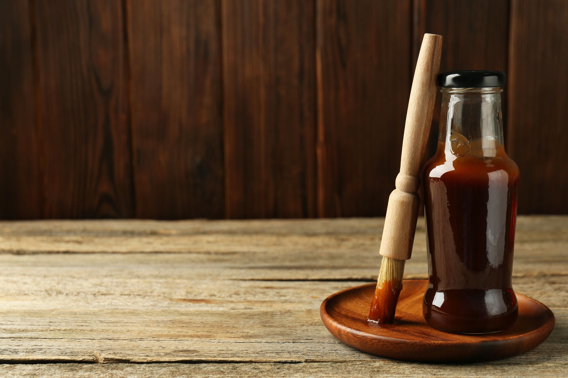 A bottle of barbecue sauce and a brush on a wooden plate on a wooden table