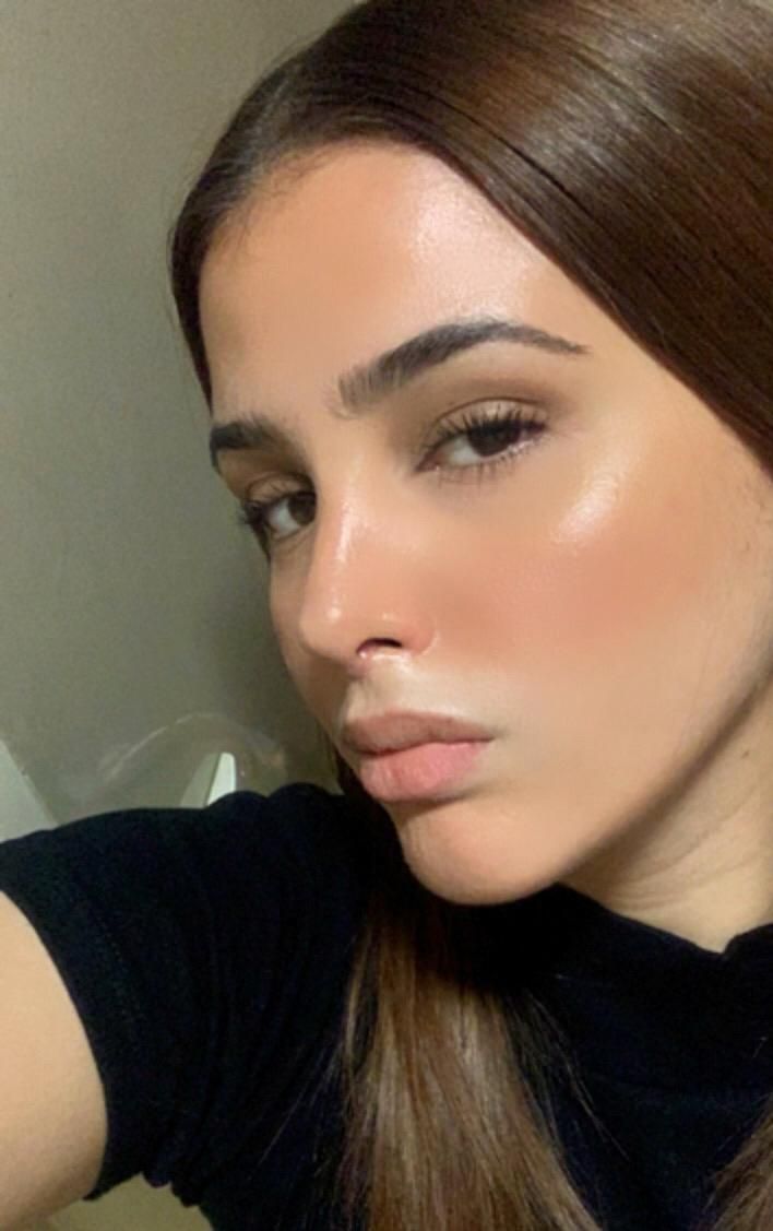 Mujer de cabello castaño y piel brillante vistiendo un top negro.