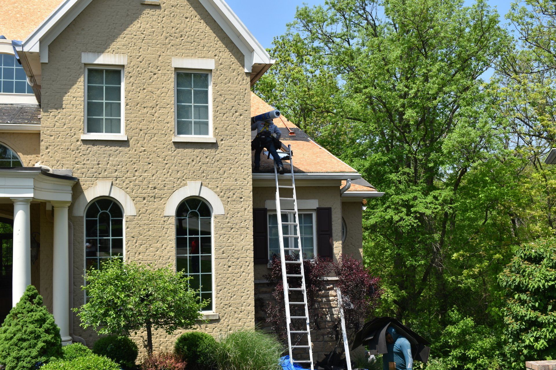 A man on a ladder is working on the roof of a house.