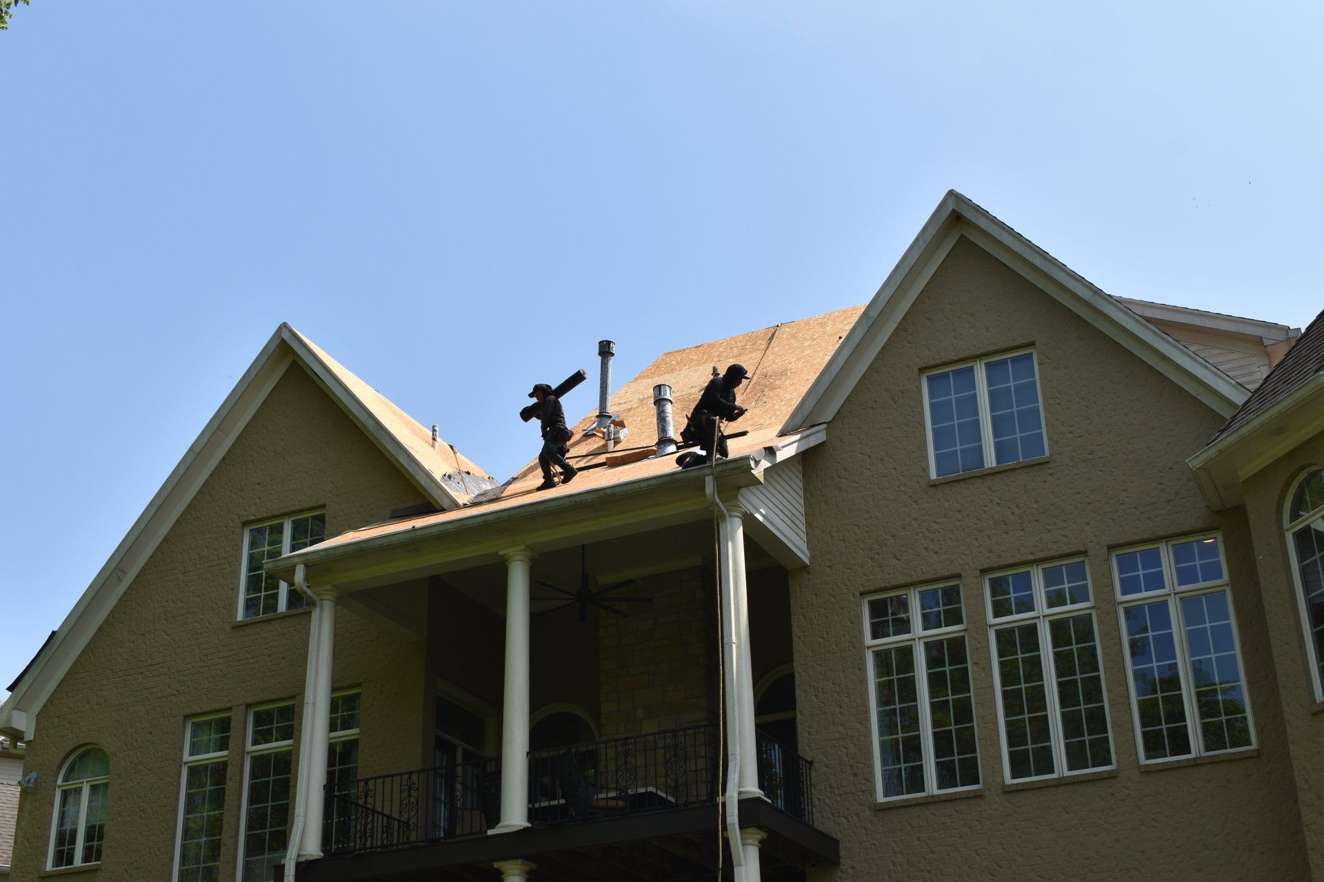 Two men are working on the roof of a large house.
