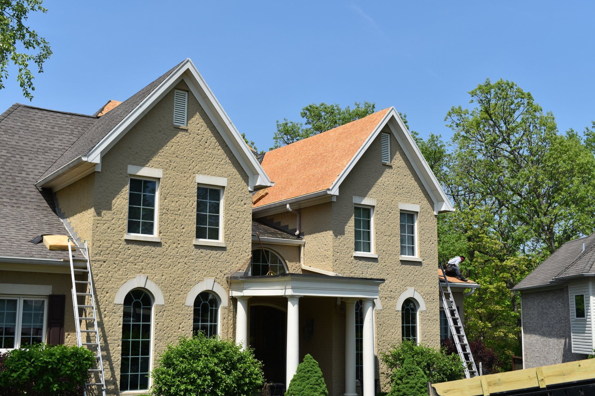 A large brick house with a roof that is being painted.