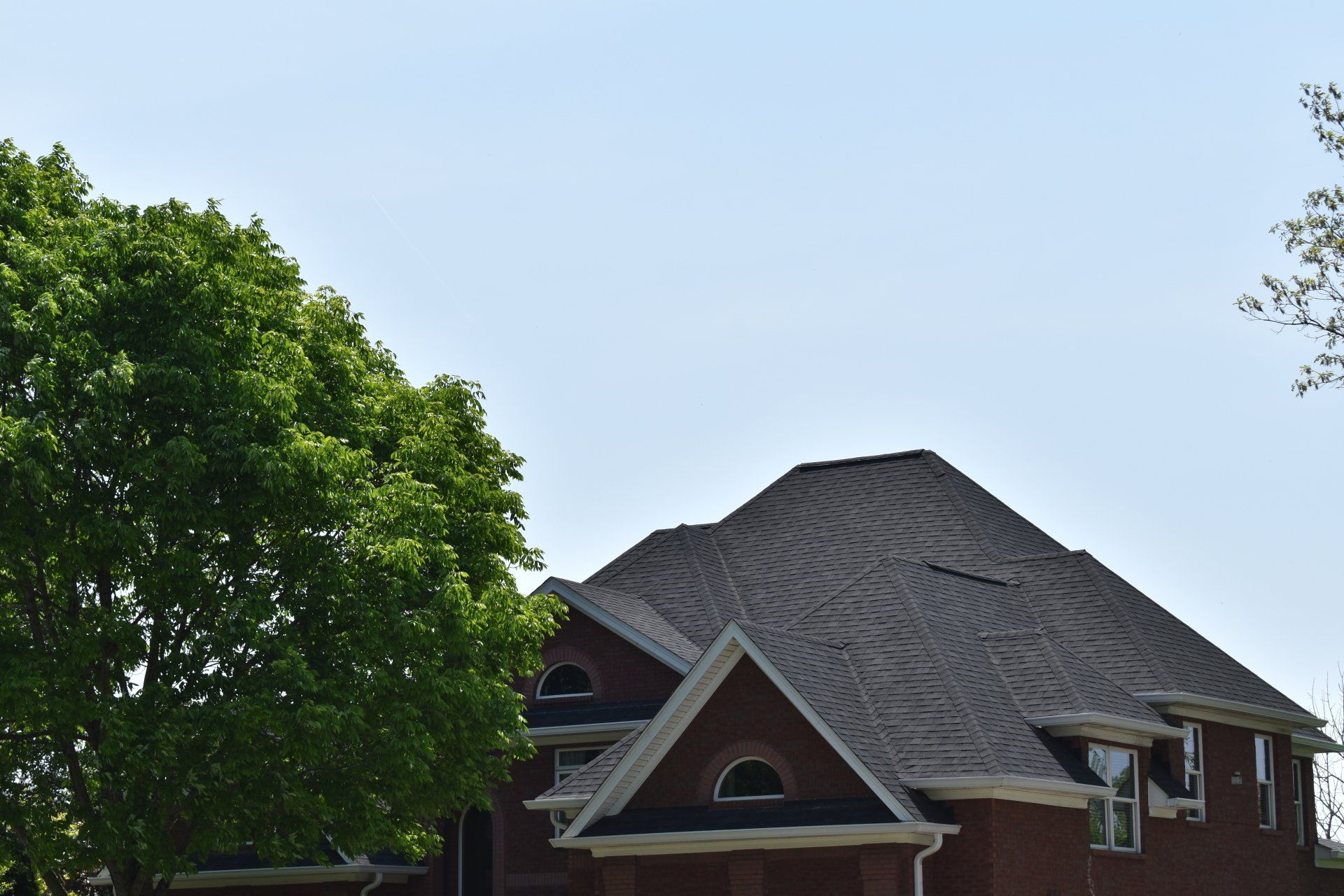 A large brick house with a black roof and a tree in front of it.