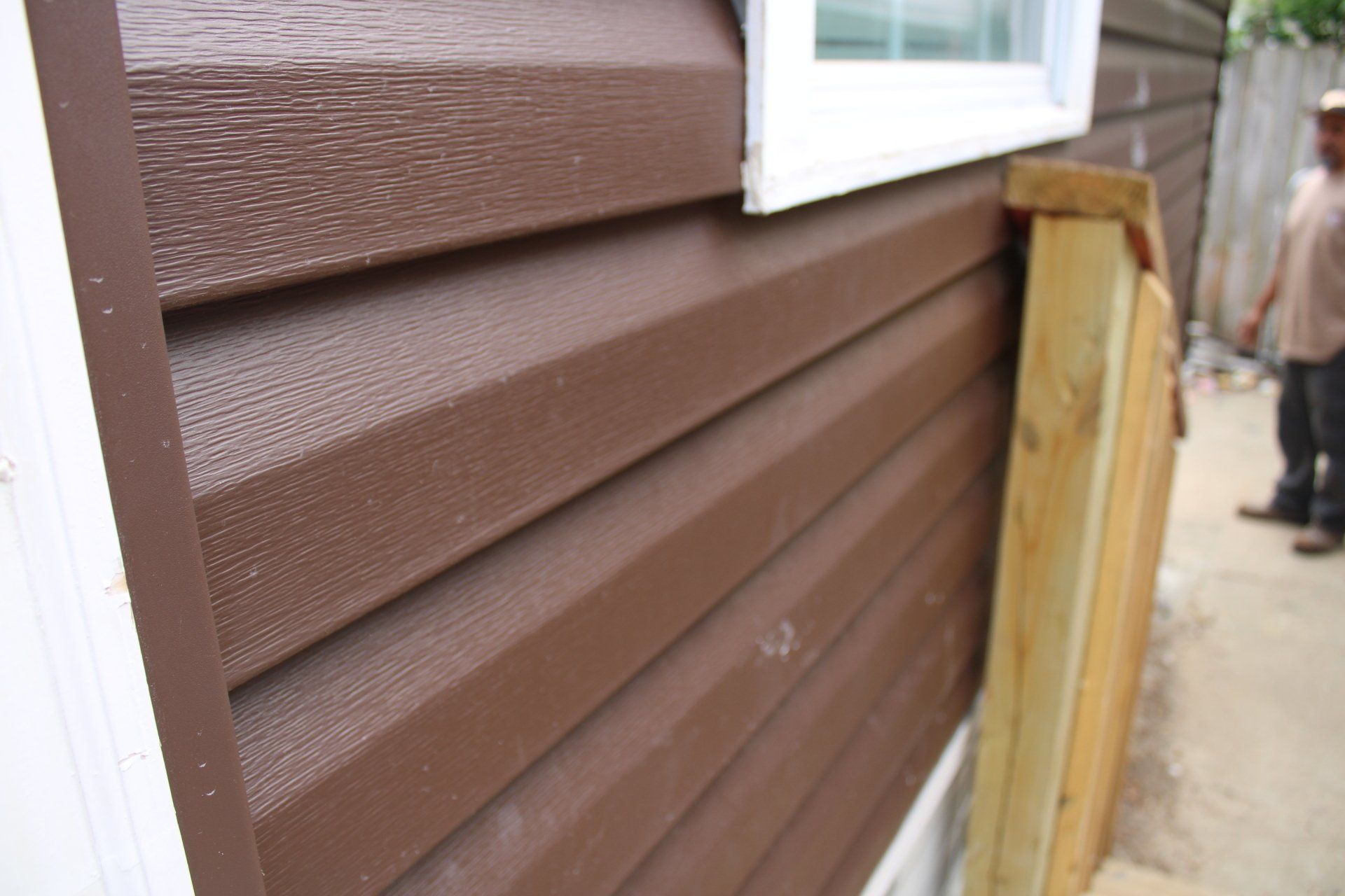 The side of a brown house with a window and a wooden fence.