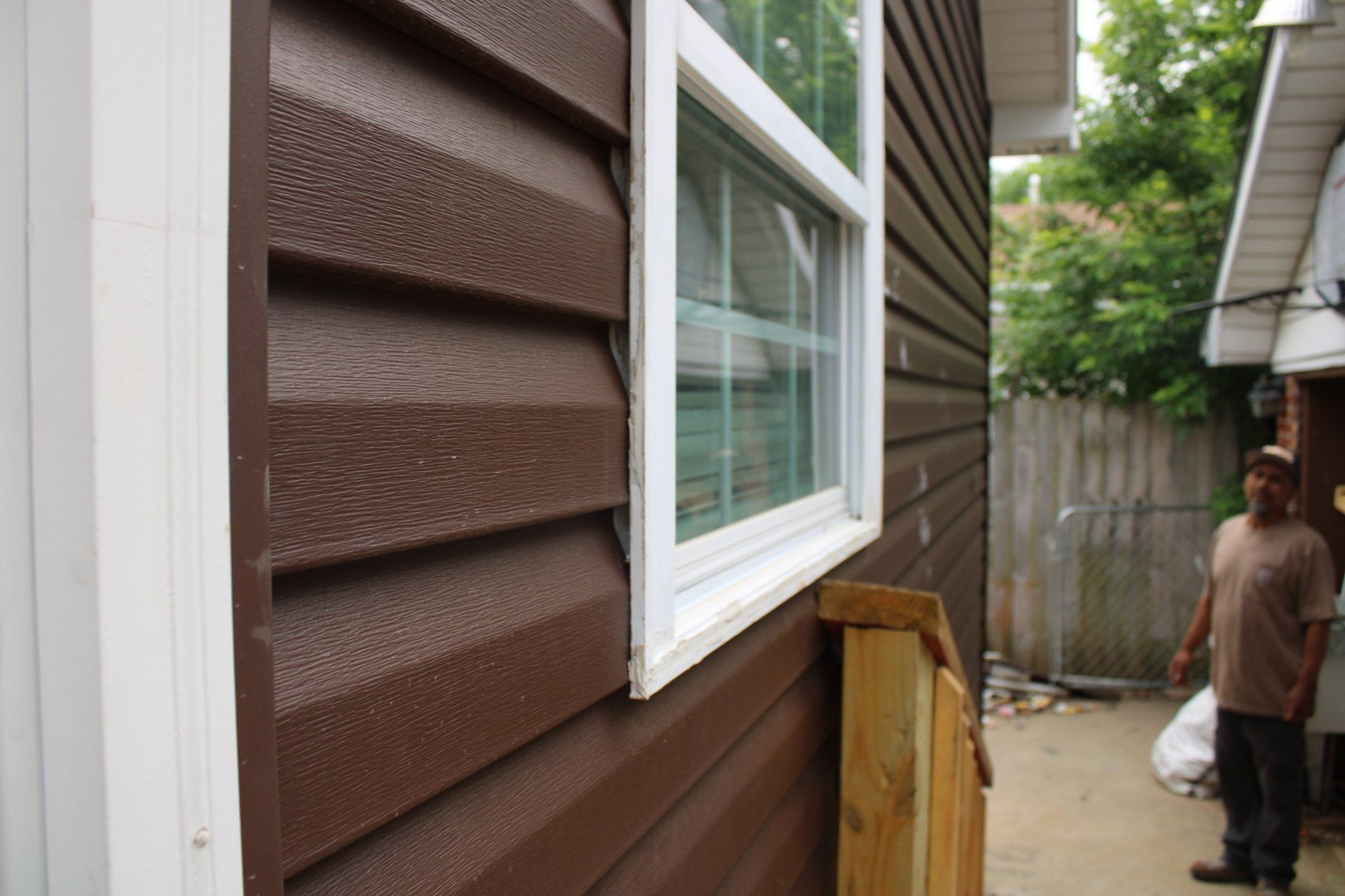 A man is standing in front of a brown house with a window